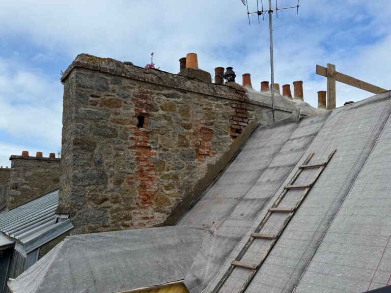 Souche de cheminée en brique fissurée et envahie de mousse à rénover, avec accès par échelle de couvreur, dans les Côtes-d'Armor.