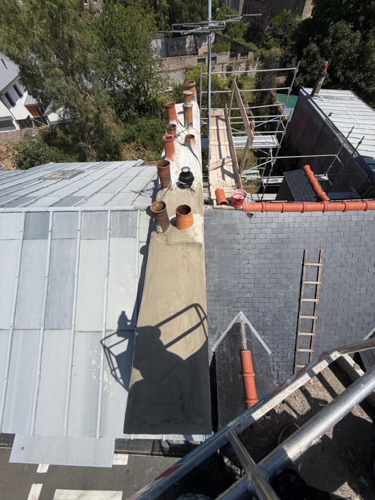 Chantier de rénovation de souche de cheminée sur une toiture en ardoise à Saint-Brieuc, avec échafaudage et protection de la couverture.
