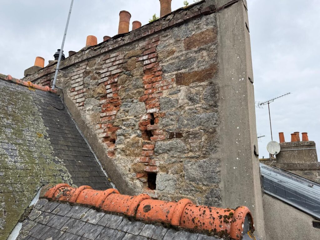 Souche de cheminée en pierre et brique fortement dégradée, joints creusés et briques déchaussées, avant réfection par Réno Habitat à Saint-Brieuc.